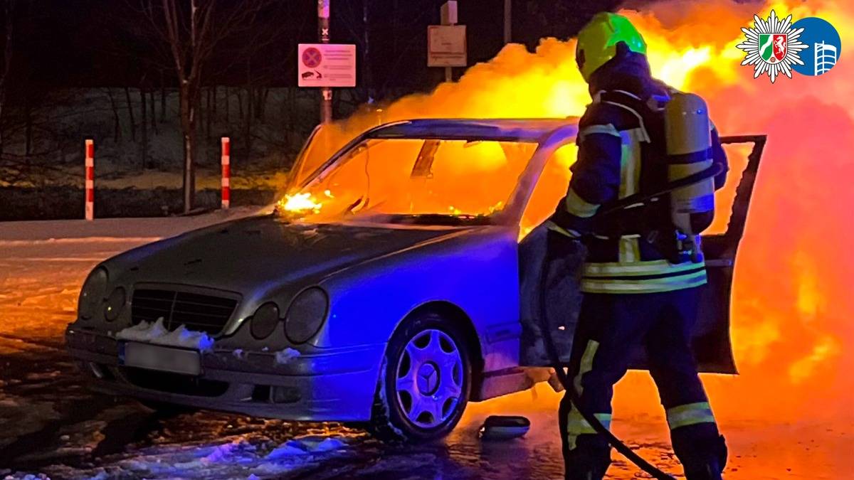 Samoch&oacute;d osobowy objęty płomieniami, obok strażak w akcji.