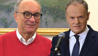 Dw&oacute;ch mężczyzn, jeden w czerwonym swetrze i okularach, drugi w garniturze i krawacie, stoją obok siebie.