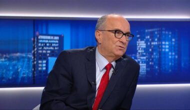 Mężczyzna w okularach i garniturze z czerwonym krawatem udziela wywiadu.