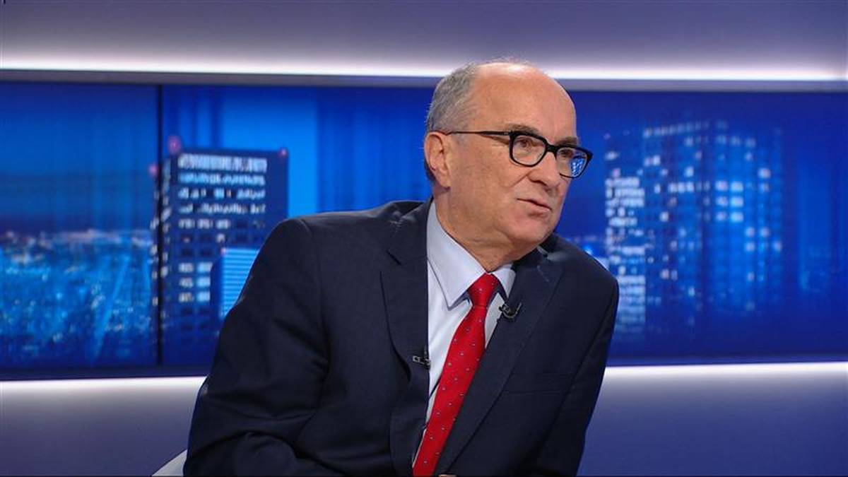 Mężczyzna w okularach i garniturze z czerwonym krawatem udziela wywiadu.