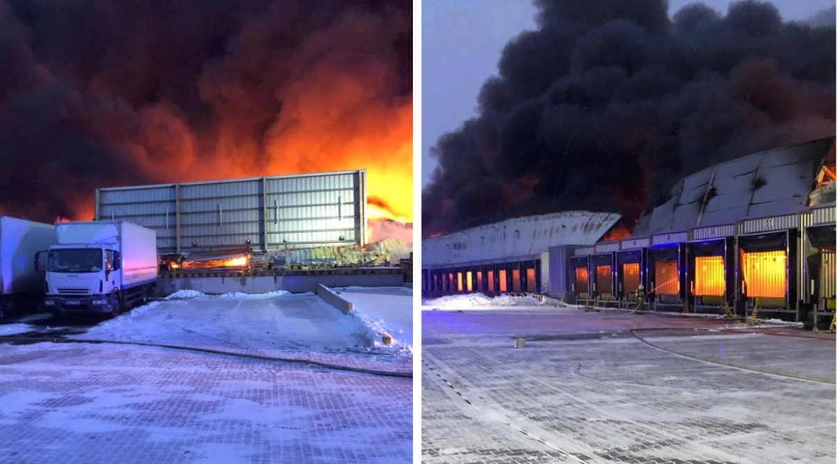 Pożar hali magazynowej z gęstym dymem i płomieniami, widoczna ciężar&oacute;wka i doki załadunkowe.