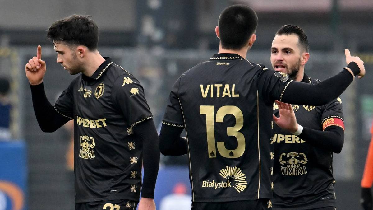 Trzech piłkarzy w czarnych strojach z numerami na plecach podczas meczu piłkarskiego.