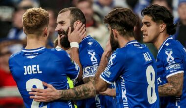 Piłkarze w niebieskich strojach piłkarskich obejmują się i rozmawiają na boisku.