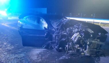 Rozbity samoch&oacute;d na poboczu drogi nocą, oświetlony światłami.