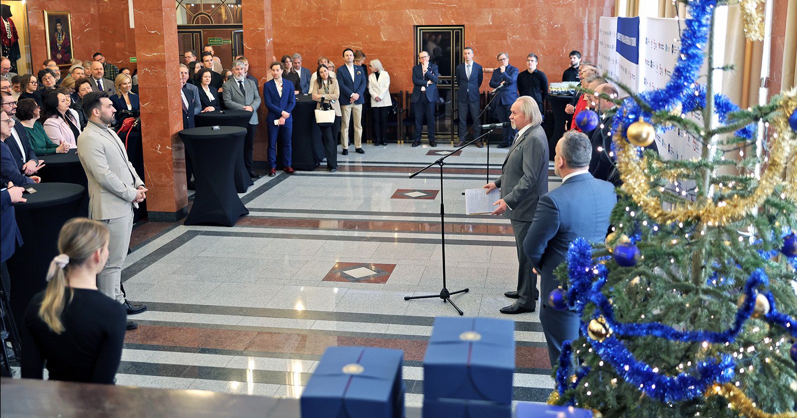 Spotkanie noworoczne było okazją do podsumowania 2025 roku oraz przedstawienia planów na przyszłość Zdjęcie zrobione z oddalenia, widać przemawiającego rektora i uczestników spotkania