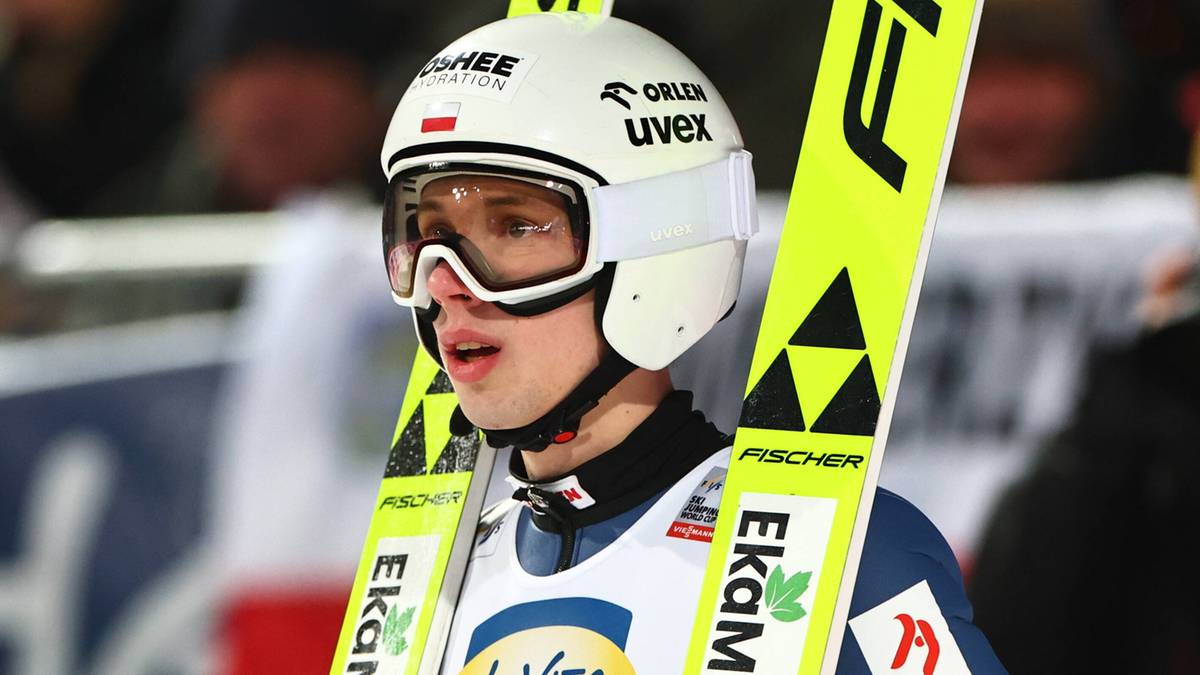 Skoczek narciarski Kacper Tomasiak w kasku i goglach narciarskich z nartami.