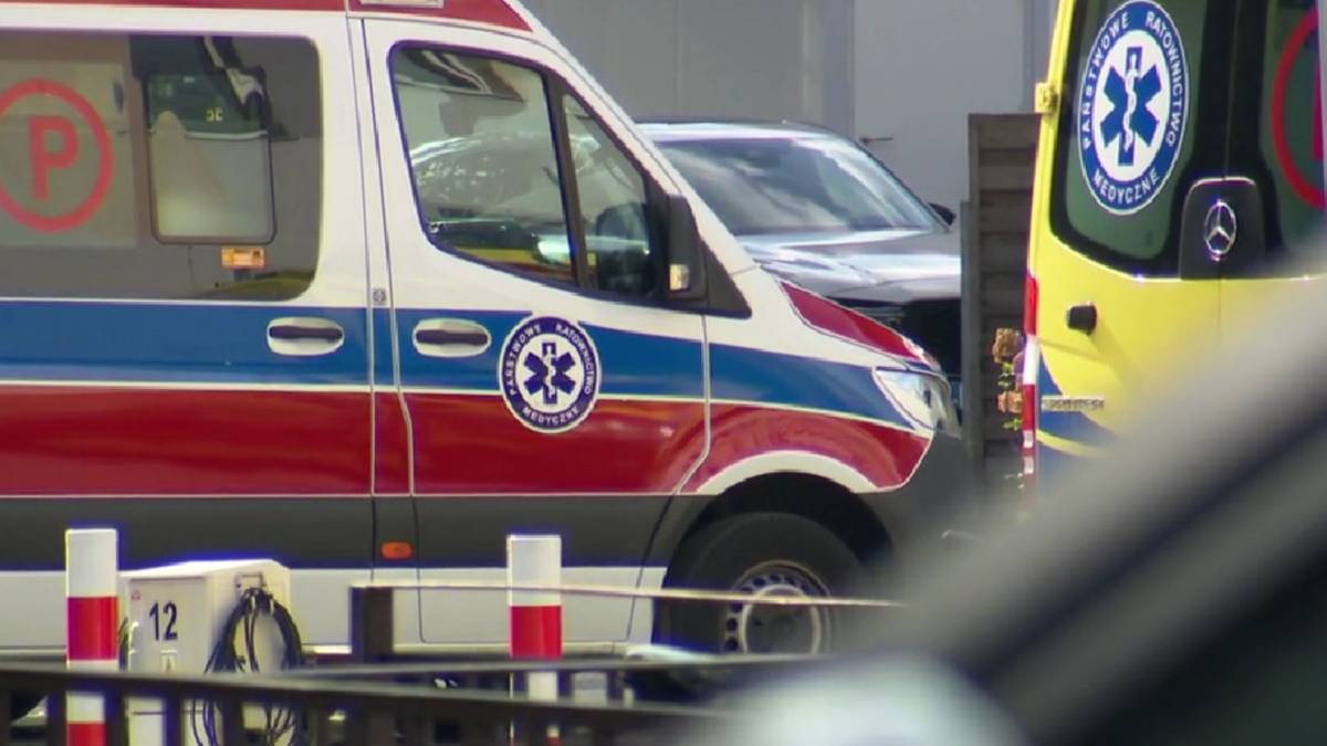 Biało-czerwono-niebieska karetka z symbolem ratunkowym na drzwiach, obok fragment ż&oacute;łtej karetki