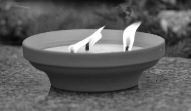 Dwa płonące znicze w misie na kamiennym tle.