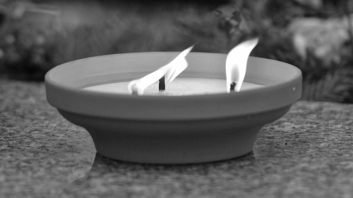 Dwa płonące znicze w misie na kamiennym tle.