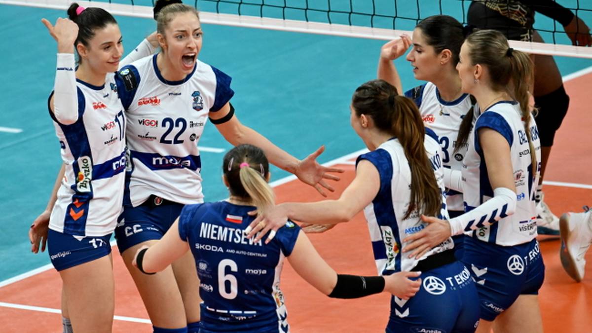 Grupa siatkarek w niebiesko-białych strojach świętująca na boisku.