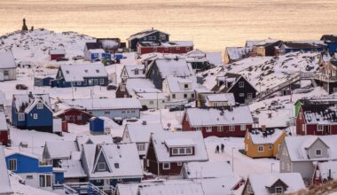 Ośnieżone wzg&oacute;rza z kolorowymi domami, widok na wodę w tle.
