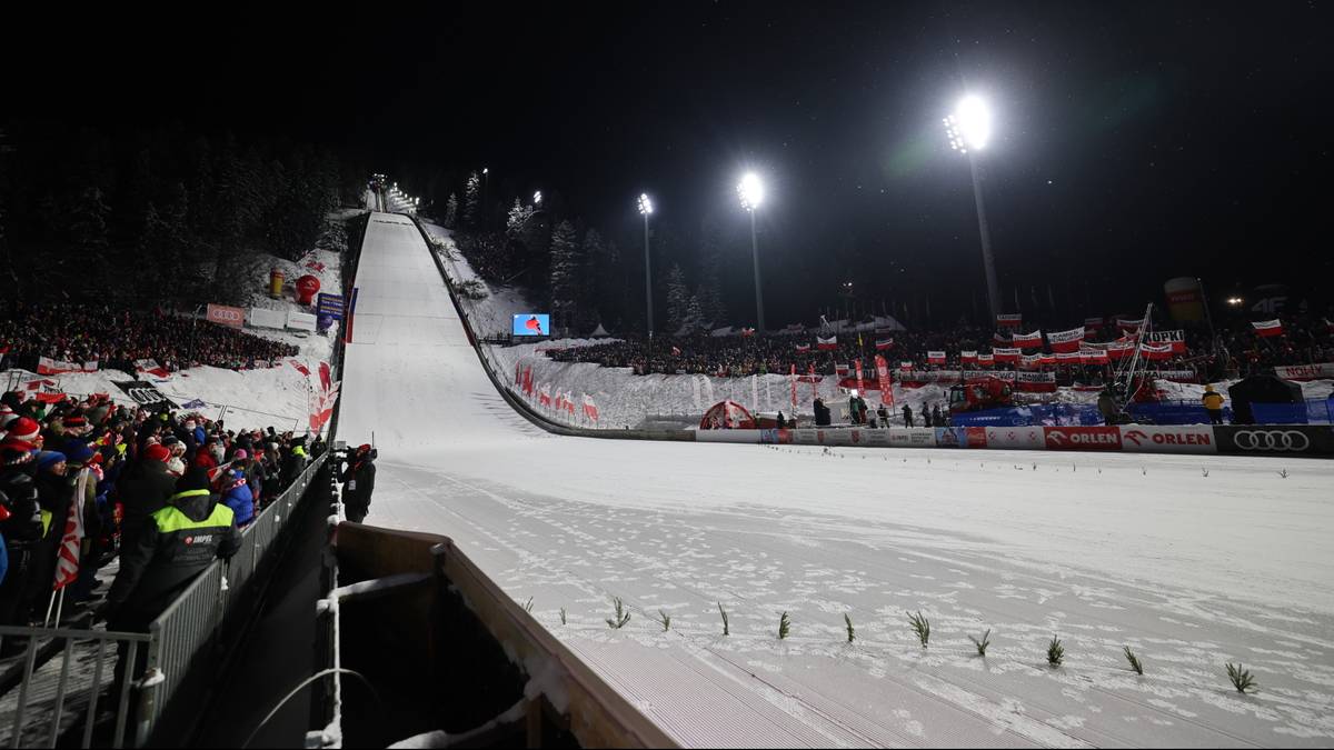 Skocznia narciarska nocą z oświetlonymi trybunami i widzami