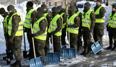 Żołnierze w kamizelkach odblaskowych i mundurach trzymają łopaty, gotowi do odśnieżania.