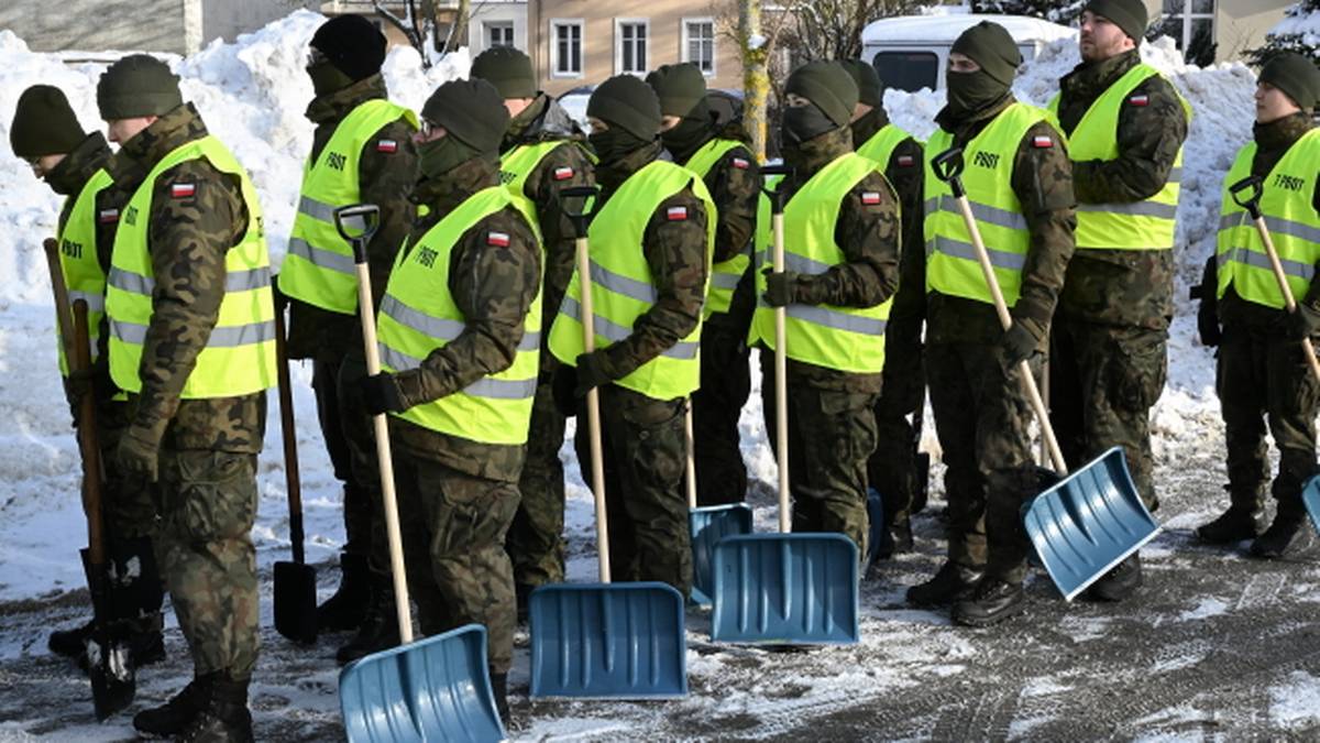Żołnierze w kamizelkach odblaskowych i mundurach trzymają łopaty, gotowi do odśnieżania.