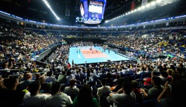 Widok na pełną widz&oacute;w halę sportową z boiskiem do siatk&oacute;wki i telebimem nad nim.