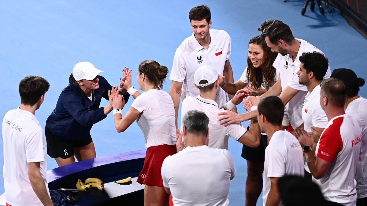 Grupa tenisist&oacute;w i trener&oacute;w celebrująca na korcie tenisowym po meczu.