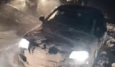 Samoch&oacute;d osobowy częściowo zasypany śniegiem, z przodu widoczny ciągnik pomocy drogowej w nocy.