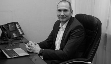 Mężczyzna w garniturze siedzi przy biurku z laptopem i telefonem.