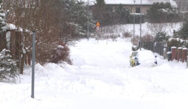 Zasypana śniegiem ulica z zaparkowanym samochodem i znakiem drogowym.