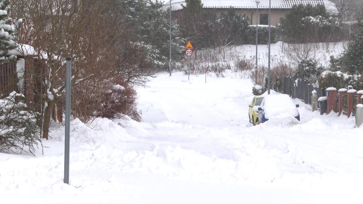 Zasypana śniegiem ulica z zaparkowanym samochodem i znakiem drogowym.