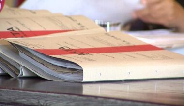 Stos papierowych dokument&oacute;w w teczkach, z czerwonym paskiem.