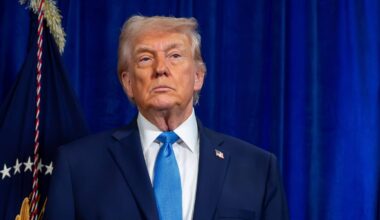 Donald Trump w garniturze i niebieskim krawacie stoi przed niebieską zasłoną.