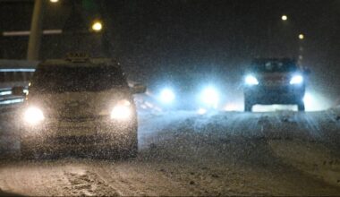 Samochody jadące po zaśnieżonej drodze nocą, światła reflektor&oacute;w oświetlają padający śnieg.