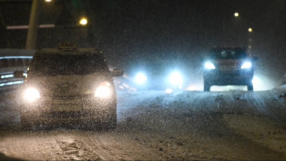 Samochody jadące po zaśnieżonej drodze nocą, światła reflektor&oacute;w oświetlają padający śnieg.