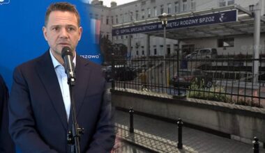 Mężczyzna w garniturze przed mikrofonem, w tle budynek szpitala.