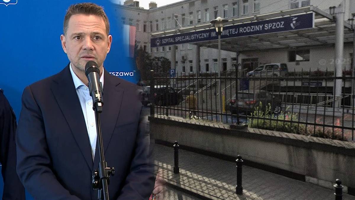 Mężczyzna w garniturze przed mikrofonem, w tle budynek szpitala.