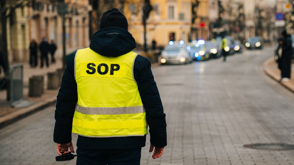 Funkcjonariusz SOP w kamizelce odblaskowej z napisem "SOP" na plecach stoi na ulicy.