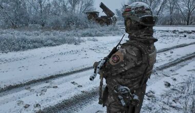 Żołnierz w zimowym kamuflażu stoi na zaśnieżonej drodze, trzymając broń.