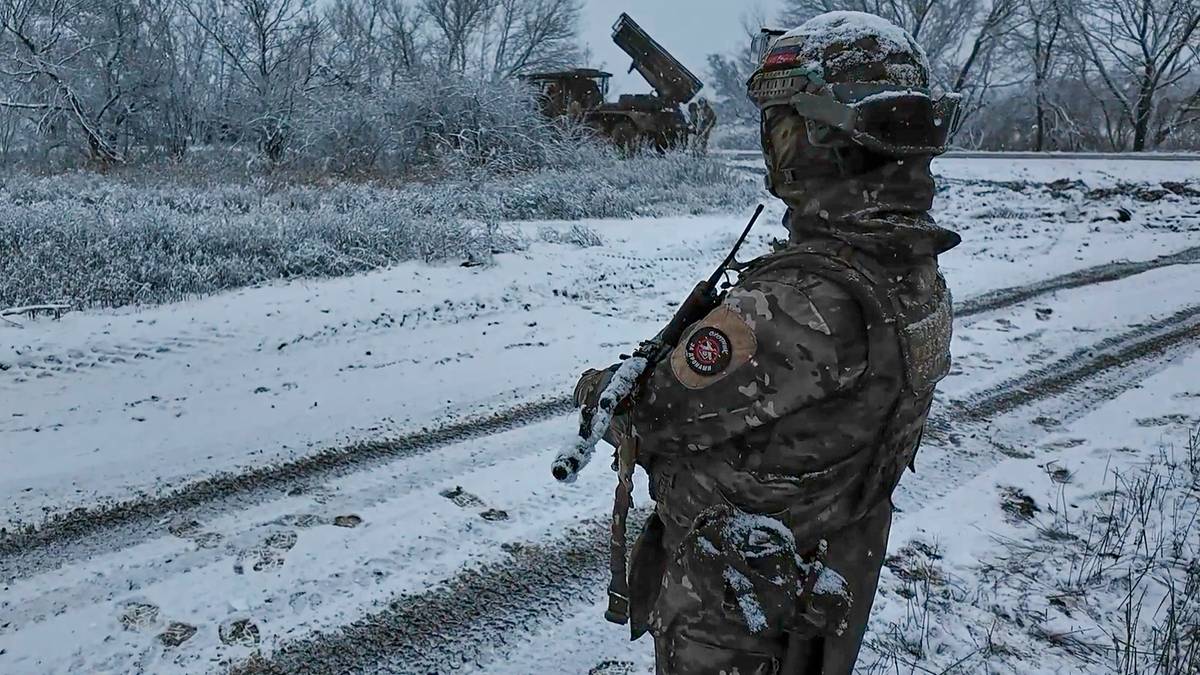 Żołnierz w zimowym kamuflażu stoi na zaśnieżonej drodze, trzymając broń.
