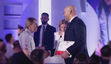 Mężczyzna w garniturze wręcza kobiecie dokument w ramce podczas oficjalnej ceremonii.