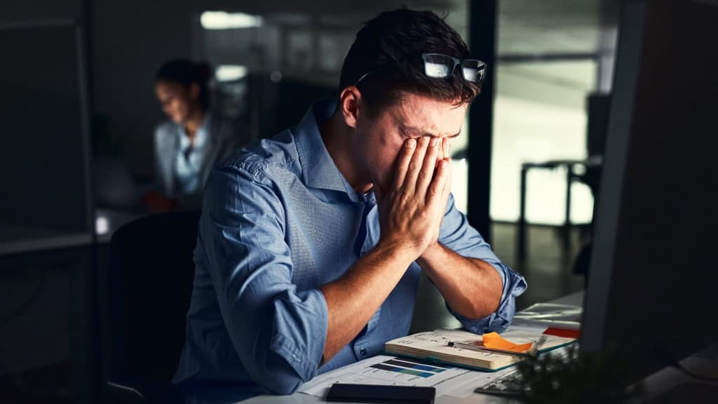 Homem estressado no escritório com rosto enterrado nas mãos