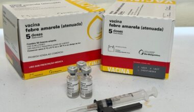 A imagem mostra duas caixas de vacina contra a febre amarela (atenuada), juntamente com três frascos-ampola e uma seringa. *Detalhes nas caixas:* * *Nome do produto:* Vacina febre amarela (atenuada) * *Quantidade:* 5 doses / frasco-ampola * *Conteúdo:* Contém 50 frascos-ampola * *Via de administração:* USO SUBCUTÂNEO * *Indicação:* USO ADULTO E PEDIÁTRICO ACIMA DE 9 MESES * *Armazenamento:* Conservar entre 2 °C e 8 °C ou a -20 °C e ao abrigo da luz. * *Restrição de venda:* PROIBIDA VENDA AO COMÉRCIO * *Prescrição:* USO SOB PRESCRIÇÃO MÉDICA * *Fabricante:* FIOCRUZ - Fundação Oswaldo Cruz, Instituto de Tecnologia em Imunobiológicos - Bio-Manguinhos. * *Informações de fabricação/lote:* F 1024 V 1027 L 240VFA036W *Frascos-ampola e seringa:* * Três frascos-ampola de vidro, com rótulos que indicam "Vacina febre amarela (atenuada)" e "5 doses". * Uma seringa descartável com uma agulha acoplada.