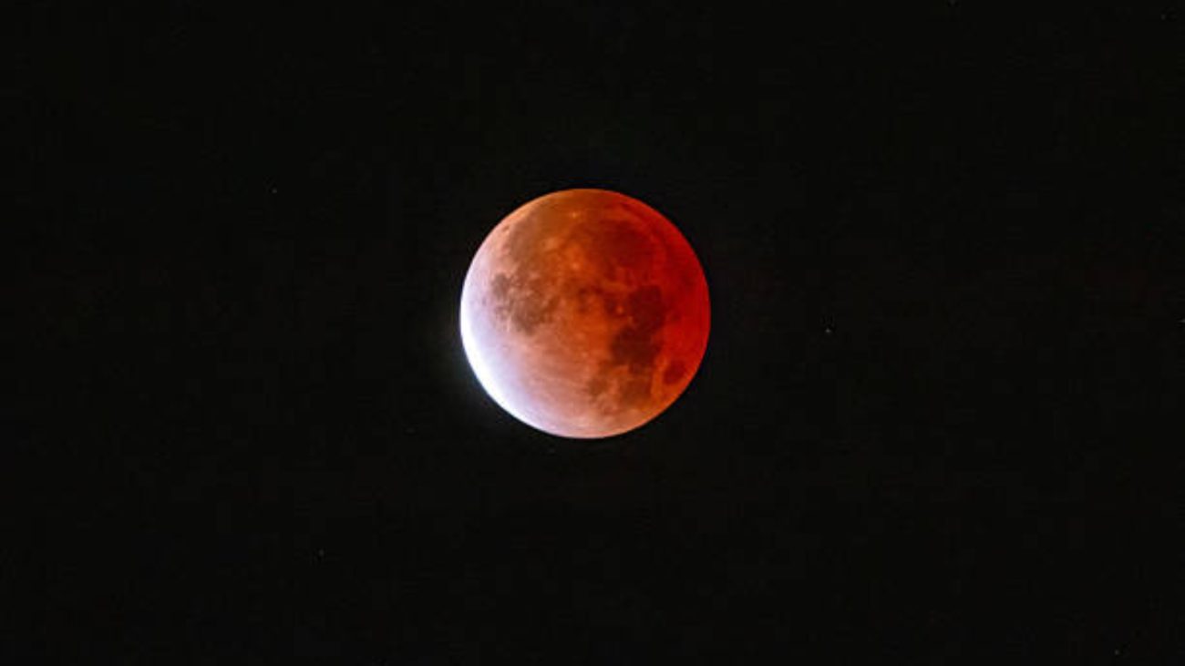 Imagem de um eclipse lunar total com a Lua parcialmente iluminada e com tonalidade avermelhada, destacando-se no céu escuro.