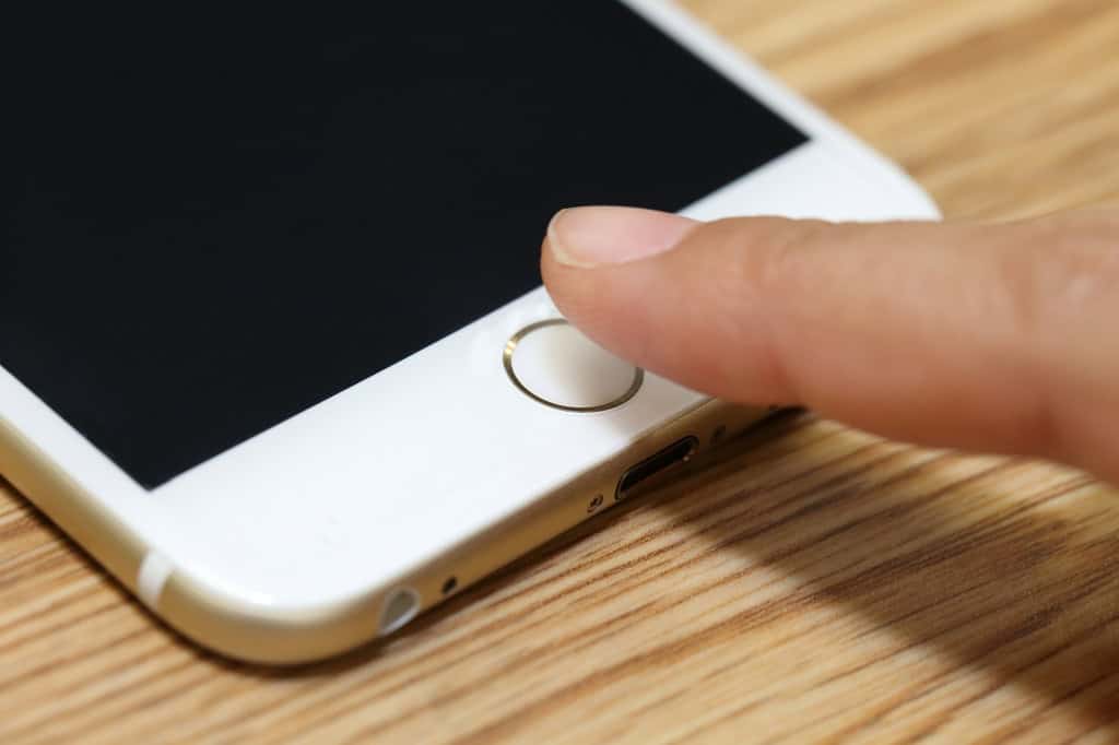 Dedo de uma pessoa pairando sobre o botão Home de um iPhone branco