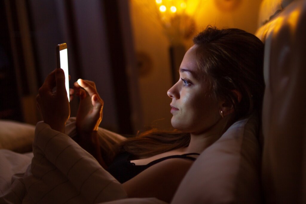 Mulher deitada na cama com o celular na mÃ£o antes de dormir