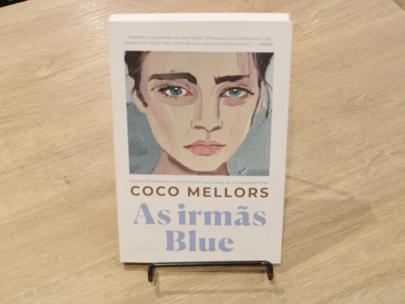 Livro "Irmãs Blue!, da autora Coco Mellors, em uma mesa.