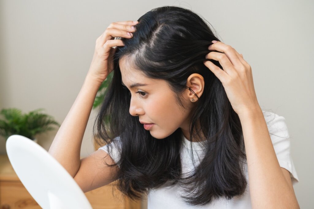 Mulher com cabelo longo e preto, olhando o couro cabeludo em um espelho