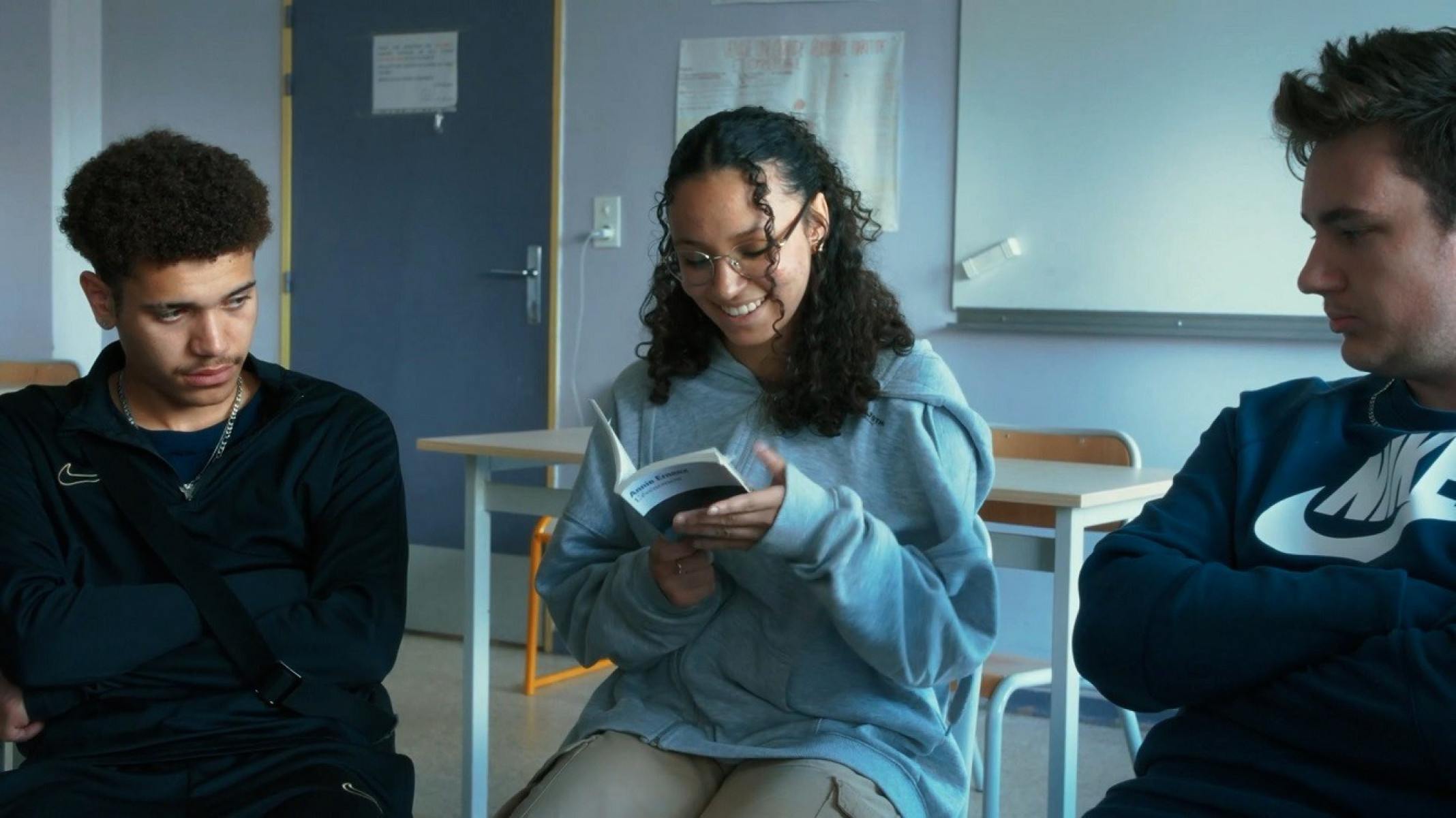 Garota lê livro e sorri, ladeada por dois adolescentes, em cena do filme Ecrire la vie 