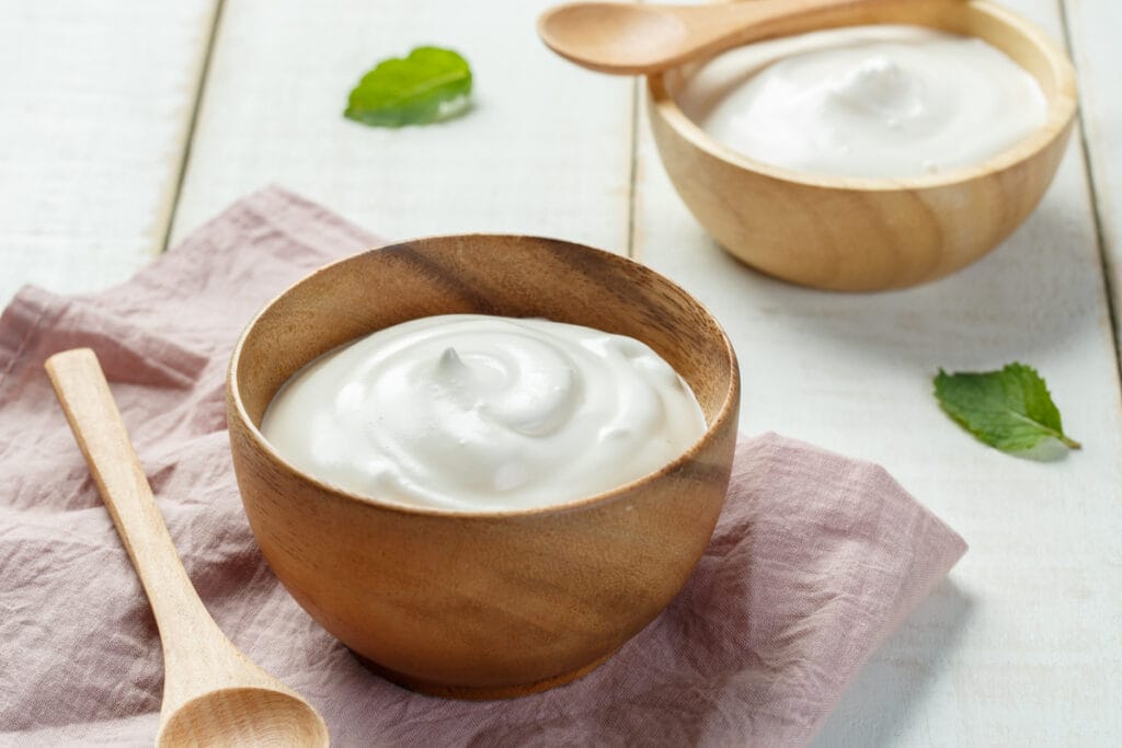 Recipiente de madeira com iogurte branco em cima de uma mesa