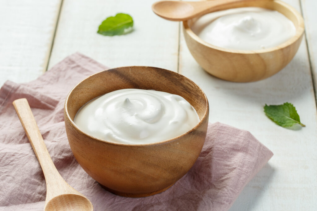 Recipiente de madeira com iogurte branco em cima de uma mesa