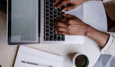 Uma pessoa a tirar notas: veem-se umas mãos em posição de digitação sobre um teclado de um computador portátil. Ao lado, um café e uma bloco de notas físico.