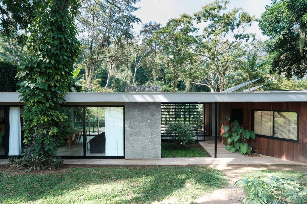 Árvore marca transição entre área social e íntima nesta casa no mato. Projeto de Thimi Arquitetura.