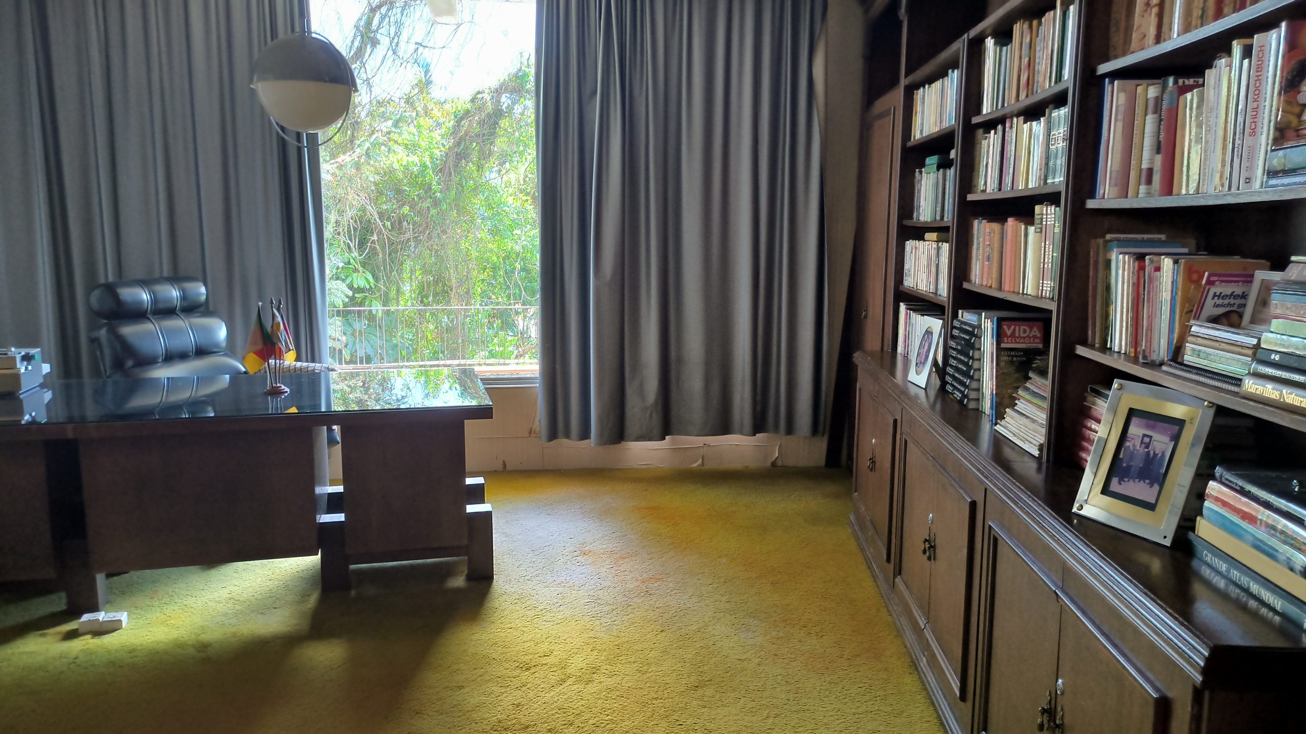 Escritório da Casa Redonda com mesa de vidro e biblioteca de madeira