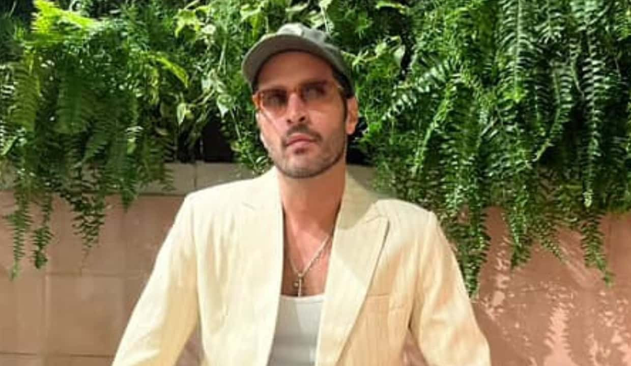 Leandro Lima de óculos escuros e boné, sério, sentado perto de plantas