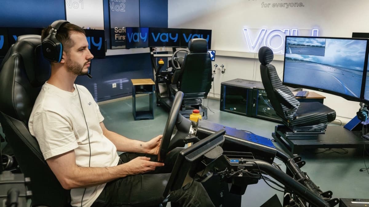 Condutor remoto da Vay, a operar um carro, por via de um volante e com auriculares. À sua volta, vários ecrãs, onde se lê "VAY" e cadeiras gaming