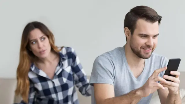 Esposa desconfiada discute com o marido que segura o celular.